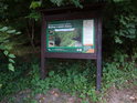 Informační cedule k chráněnému území na okraji smíšeného lesa.