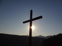 Slunce klesá za srpnového včera za levý kříž na Kalvárii, kopce v pozadí jsou Lovoš a Milešovka.
