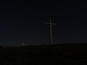Velký ocelový kříž na vrcholu Radobýlu pod hvězdami uprostřed noci.
