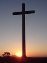 Ocelový kříž na vrcholu Radobýlu při vycházejícím Slunci na jižní straně kopce Bídnice.