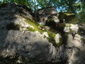 Menší skalní stěna osvětlená slunečními paprsky, které pronikly mezi listy stromů.